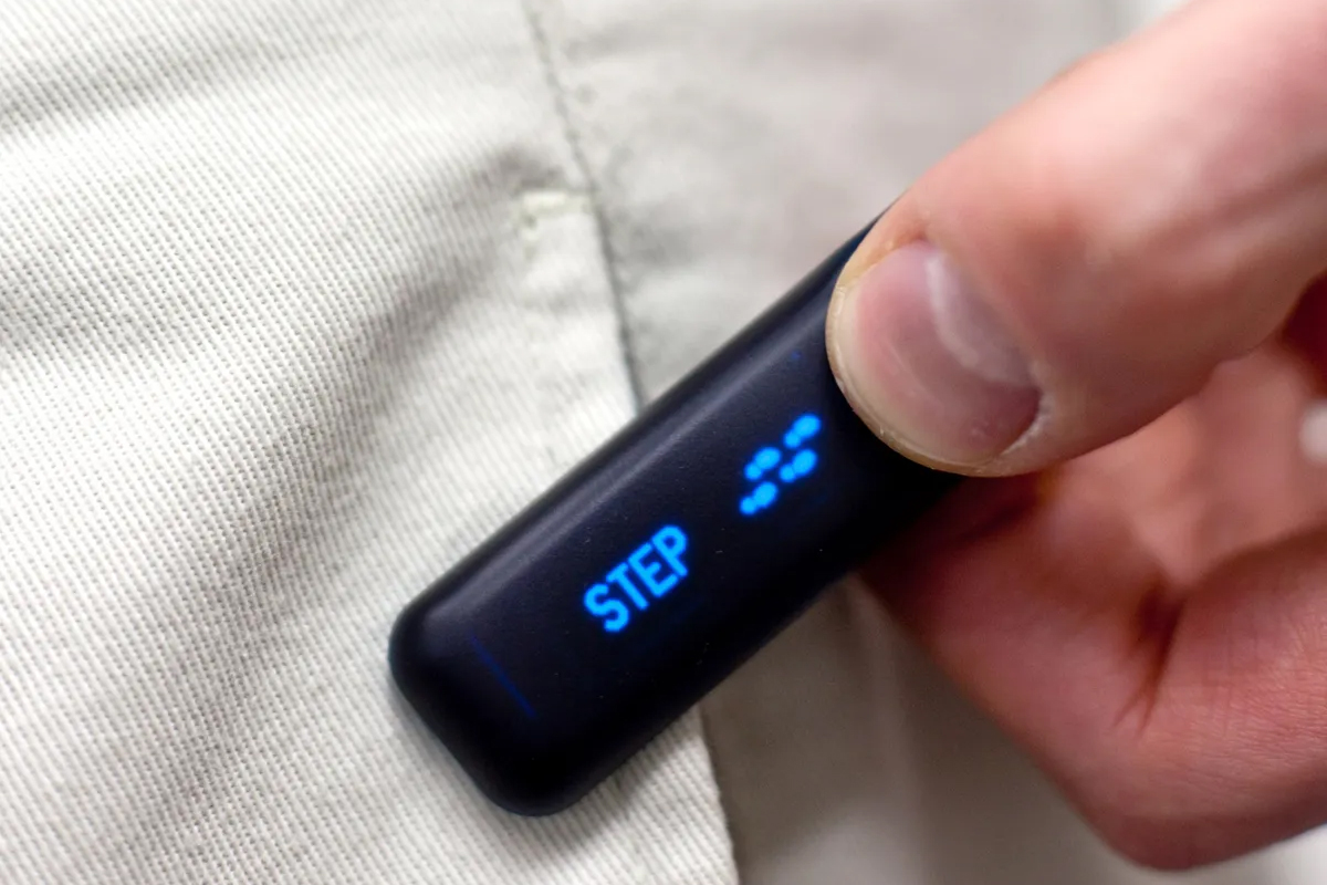 Fingers holding an active FitBit device.