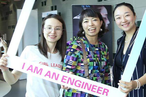 Three women stand in a photograph frame smiling. The frame has the words I Am an Engineer on it.